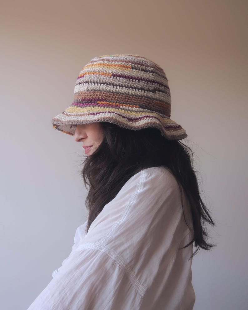 May include: A crocheted bucket hat with a striped pattern in shades of brown, beige, yellow, and purple.