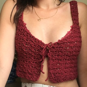 May include: A burgundy crochet top with a tie front and a delicate lace trim. The top is cropped and has a relaxed fit.
