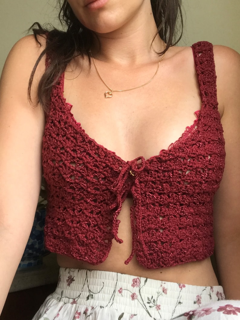 May include: A burgundy crochet top with a tie front and a delicate lace trim. The top is cropped and has a relaxed fit.