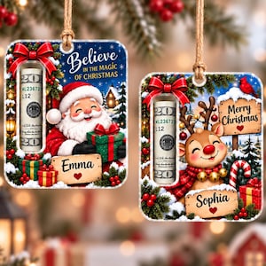 May include: Two rectangular acrylic Christmas ornaments with jute twine hangers. Each features a cylindrical slot holding a rolled twenty-dollar bill, a red bow, and festive graphics. One shows Santa with the name Emma, the other a reindeer with the name Sophia.