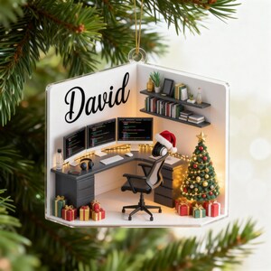 May include: A clear acrylic Christmas ornament featuring a miniature office scene. The ornament includes a desk with three computer monitors, a Christmas tree, and the name "David". Presents and a Santa hat add festive touches.