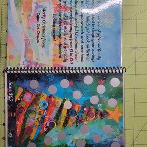 May include: A colorful Christmas-themed scratch-and-save book with a festive tree design. The book has silver circles that can be scratched to reveal discounts. The text on the book reads "Tis the season of gifts and family gathering...Want to sleigh your savings game for holidays? Look no further than this unique scratch-and-save book bursting with colorful Christmas cheer! Unwrap surprises ranging from $1 to $10 with your lucky scratcher and get ready for a festive ride through whimsical holiday scenes! Merry Christmas from: Cajun Girl Creates Save $95"