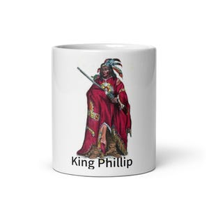 May include: White ceramic mug with a colorful illustration of King Phillip, a Native American man in traditional clothing, holding a rifle. The text "King Phillip" is printed below the image.