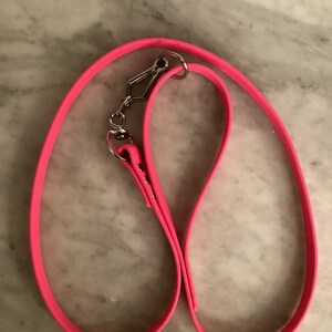 May include: Bright pink dog leash with a silver metal clasp and ring. The leash is made of a flexible, durable material. The leash is designed for pet owners to use when walking their dogs.