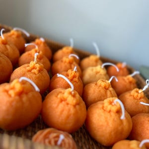 May include: A wicker basket filled with small orange candles shaped like oranges. The candles have white wicks.