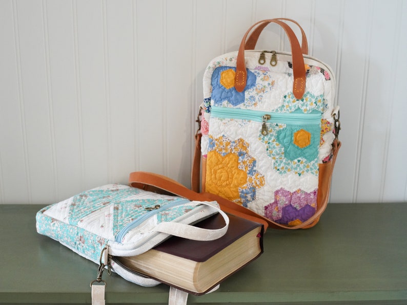 May include: Two quilted fabric bags with floral patterns and leather accents. One bag is upright with a top handle and a shoulder strap. The other bag is open, revealing a book inside. Both bags have zippered compartments.