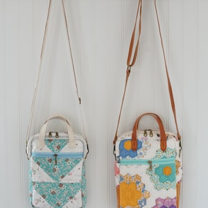 May include: Two quilted crossbody bags hanging on a wooden rack. The bag on the left has a teal and white floral pattern, while the bag on the right features a colorful floral design with orange, blue, and purple hues. Both have zippered closures and adjustable straps.