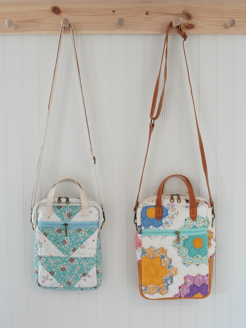 May include: Two quilted crossbody bags hanging on a wooden rack. The bag on the left has a teal and white floral pattern, while the bag on the right features a colorful floral design with orange, blue, and purple hues. Both have zippered closures and adjustable straps.