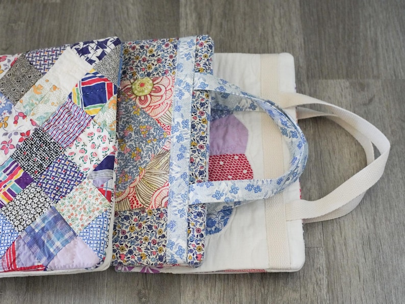 May include: A patchwork tote bag with a variety of colorful fabric patterns. The bag features a handle made of blue floral fabric and a white canvas strap. The bag is open, revealing the interior with more patchwork and a white lining.