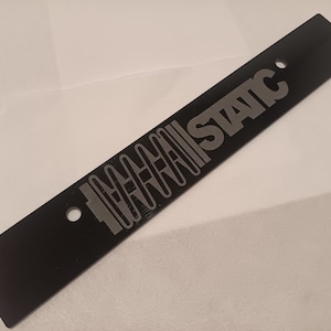 May include: A black metal license plate frame with the text "MINI STATIC" in silver lettering.