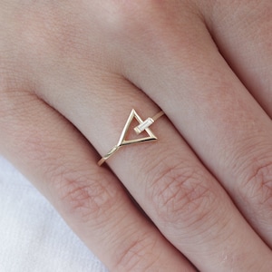 May include: A gold triangle ring with a small diamond set in the center. The ring is on a finger with light pink nail polish.