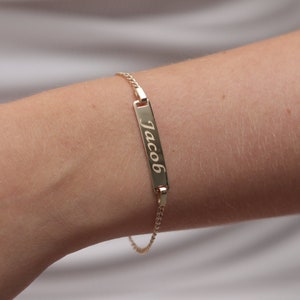 May include: A gold chain bracelet with a rectangular nameplate charm engraved with the name "Jacob".