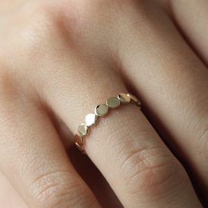 May include: A gold ring featuring a row of small, round, flat, gold discs.