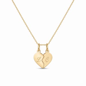 May include: A gold-toned necklace featuring a pendant composed of two separate heart halves that fit together. Each half is suspended by a small jump ring from a delicate chain and features an engraved cursive letter, L on the left and C on the right.