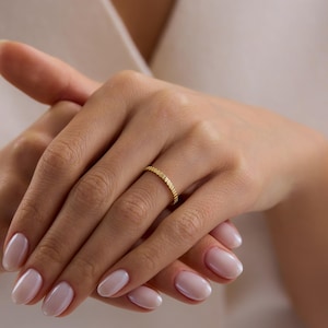 May include: A gold ring with a textured, ridged design. The ring is worn on a finger, showcasing its intricate details and warm, metallic hue. The ring's design is a continuous pattern around the band.