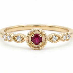 May include: A gold ring with a central round ruby gemstone, surrounded by a beaded design. The ring features small diamond accents on either side of the ruby, set in a delicate band. Jewelry.