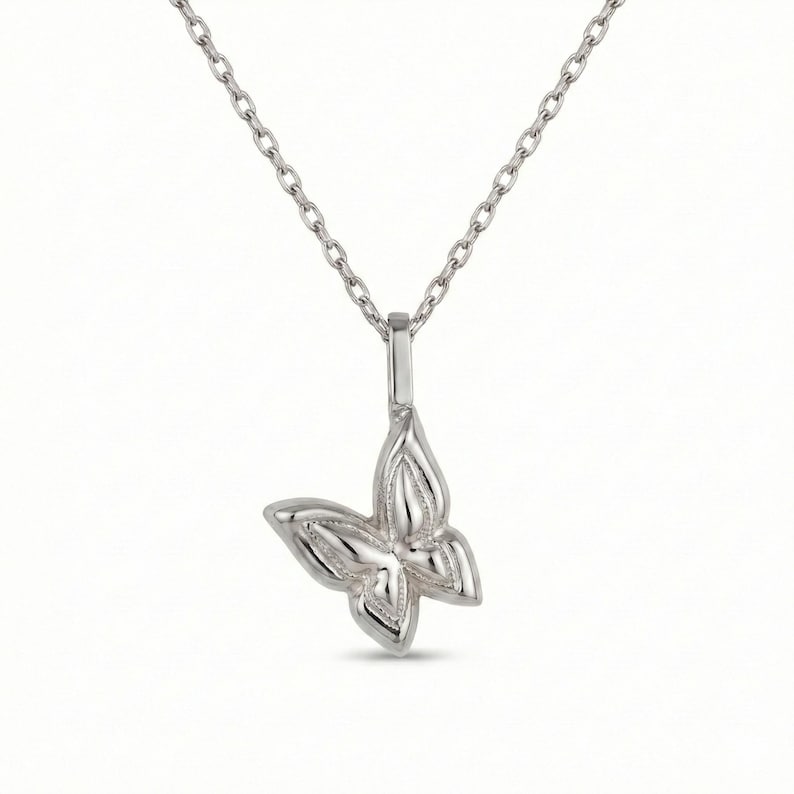 May include: A silver-colored butterfly pendant necklace. The butterfly pendant has detailed wing designs and hangs from a delicate chain. The necklace is displayed against a white background.