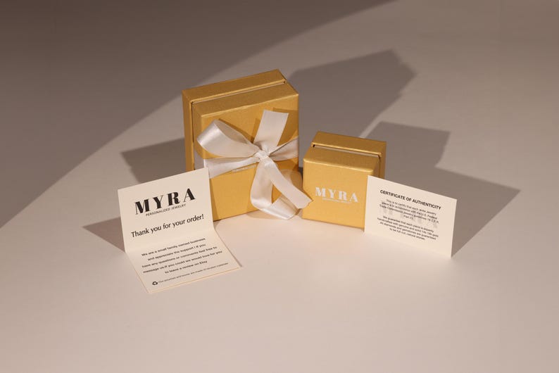 May include: A gold-colored gift box with a white ribbon bow, a smaller box, and two cards. The cards read "MYRA Personalized Jewelry" and "Thank you for your order!" and "Certificate of Authenticity".