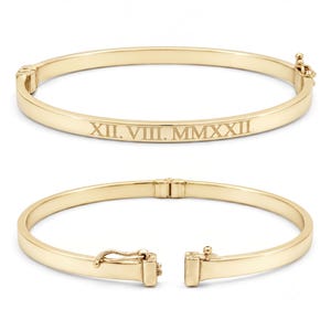 May include: A polished gold-tone hinged bangle bracelet featuring the engraved Roman numeral date XII. VIII. MMXXII on the front surface. The second view shows the same bracelet open, displaying the secure metal clasp mechanism and hinge.