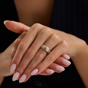 Könnte beinhalten: Ein gold-silberner Ring mit geometrischem Design. Der Ring hat eine Reihe rechteckiger Formen in abwechselnden Gold- und Silbertönen. Der Ring wird an einem Finger getragen, vor schwarzem Hintergrund.