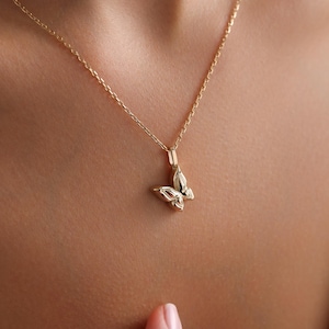 May include: A gold-colored butterfly pendant necklace. The butterfly pendant is small and detailed, with visible wings and body. The necklace chain is delicate and also gold-colored. The necklace is worn around the neck.
