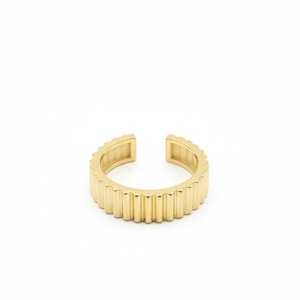 May include: A gold-colored ring with a ribbed design. The ring has an open design, with a gap at the top. The ring is made of a shiny, metallic material. The ring is a piece of jewelry.