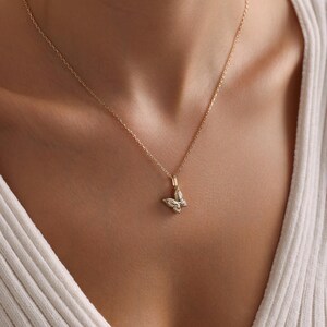 May include: A delicate gold-colored butterfly pendant necklace. The butterfly charm is intricately detailed and suspended from a fine chain. The necklace is shown against a white ribbed top.