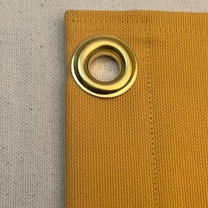 以下が含まれることがあります： マスタードイエローの生地に金色の金属製のグロメットが取り付けられています。生地は織り込まれた質感です。