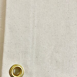 以下が含まれることがあります： 白いキャンバス生地のクローズアップ。金色の金属製のグロメットがあります。