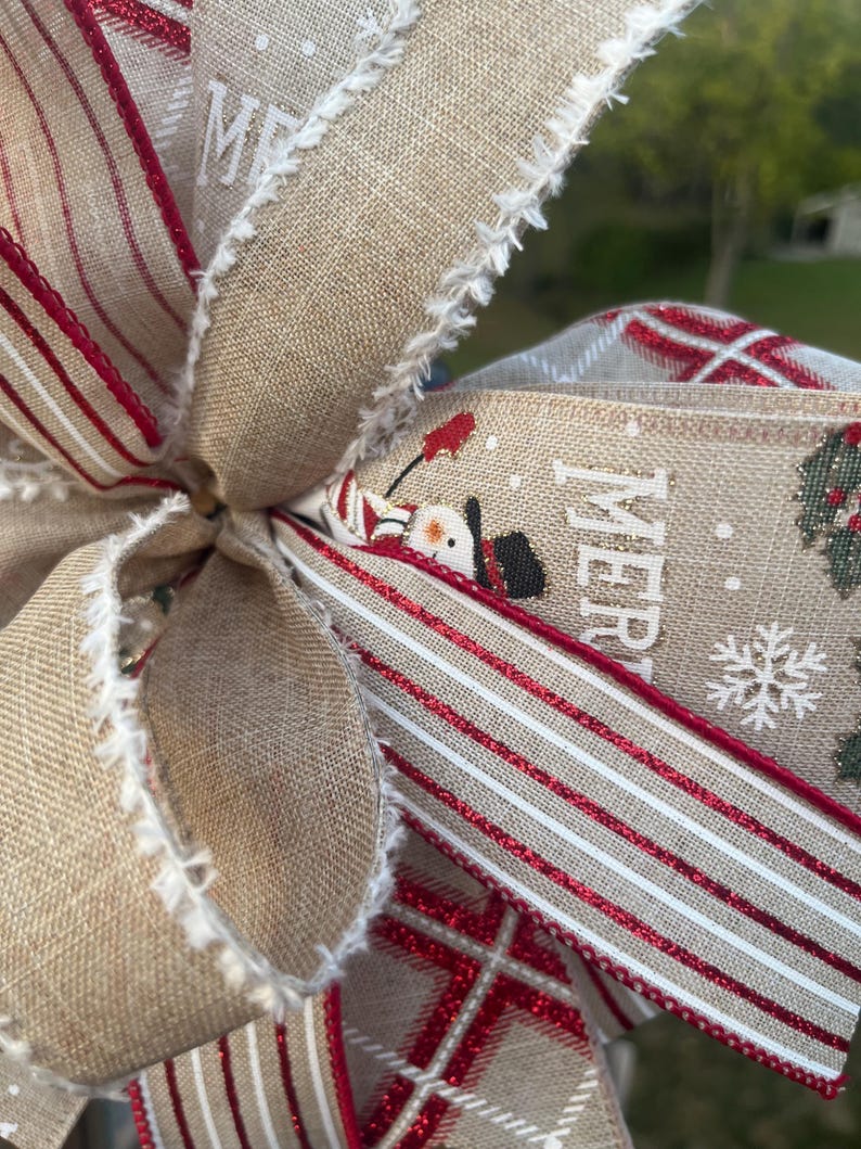 May include: A close-up of a Christmas bow made with burlap ribbon, red and white striped ribbon, and plaid ribbon. The bow has a frayed edge and features the word "Merry" printed on the ribbon.
