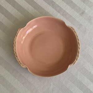 May include: A pale pink ceramic serving bowl with a rope-like design around the rim and two handles. The bowl is empty.