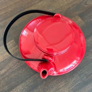 May include: A vibrant red teapot with a black handle and a matching lid. The teapot has a glossy finish and a spout for pouring. The design is simple and modern, suitable for kitchen decor.