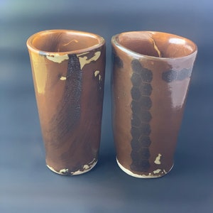 May include: Two brown ceramic mugs with different patterns. One mug has a white and brown marbled pattern, while the other has a black and brown honeycomb pattern.