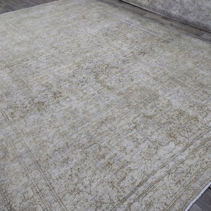 May include: A vintage rug with a light beige background and a faded floral pattern in a darker beige color. The rug has a border with a more intricate design.