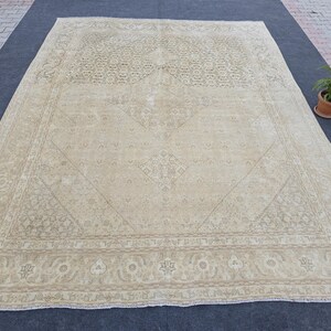 May include: A large, off-white rug with a detailed, intricate pattern. The rug has a faded, vintage look and a subtle, light brown border.