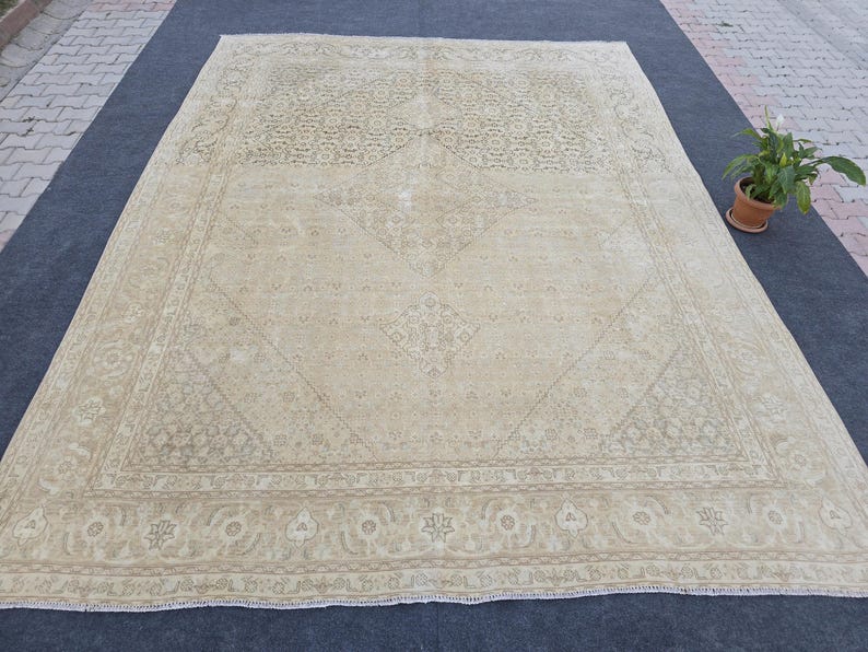May include: A large, off-white rug with a detailed, intricate pattern. The rug has a faded, vintage look and a subtle, light brown border.