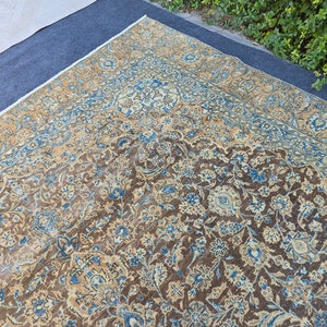 Puede incluir: Una alfombra persa vintage con un patrón floral en tonos marrones, azules y crema. La alfombra tiene un aspecto desgastado y descolorido, lo que le da un carácter único.