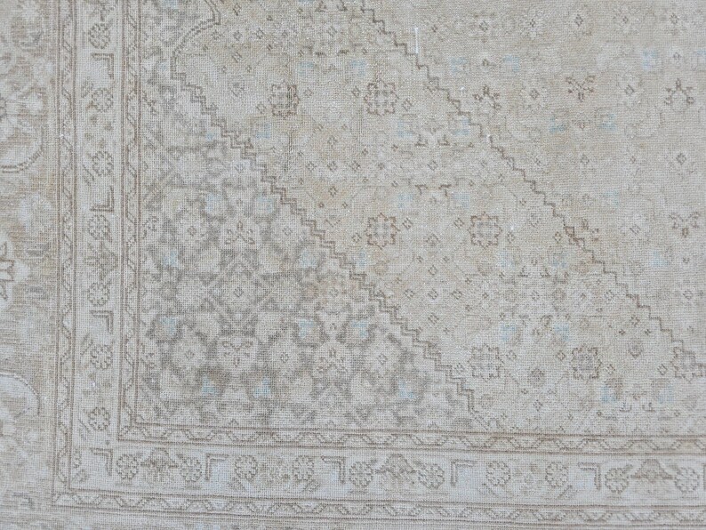 May include: A vintage rug with a faded, light beige background and a geometric pattern in shades of gray and blue. The rug has a border with a repeating design.