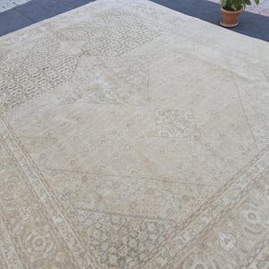 May include: A cream-colored rug with a geometric pattern. The rug has a faded, vintage look and is made of a soft, woven material.