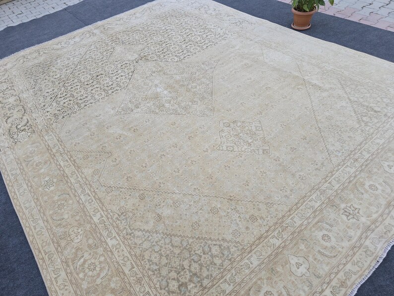 May include: A cream-colored rug with a geometric pattern. The rug has a faded, vintage look and is made of a soft, woven material.