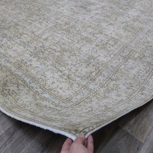 May include: A beige rug with a floral pattern and a white border. The rug is folded in half and the edge is visible.