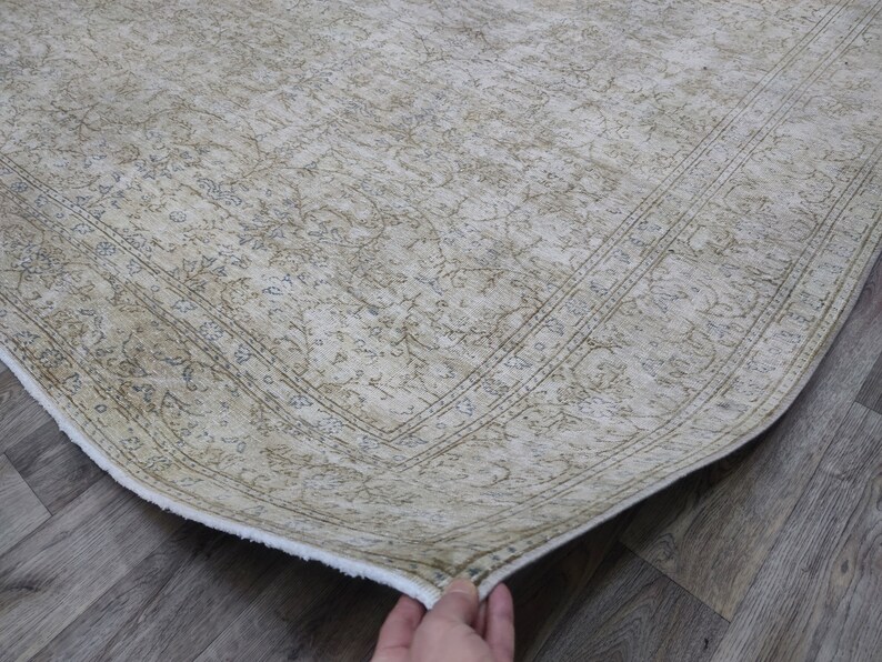 May include: A beige rug with a floral pattern and a white border. The rug is folded in half and the edge is visible.