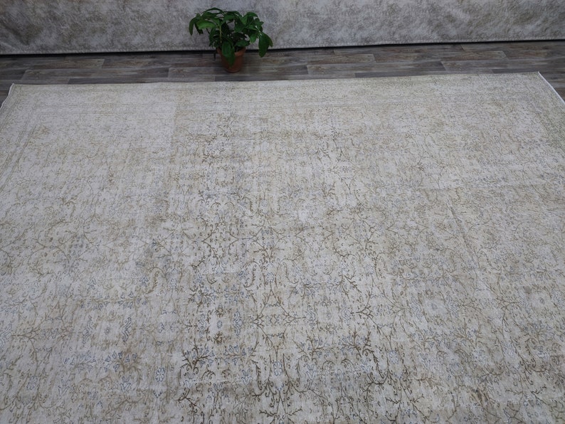 May include: A light beige area rug with a subtle, distressed floral pattern. The rug has a soft, faded look, giving it a vintage feel.