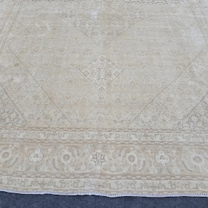 May include: A cream-colored rug with a subtle floral pattern and a border of intricate designs. The rug has a fringed edge.