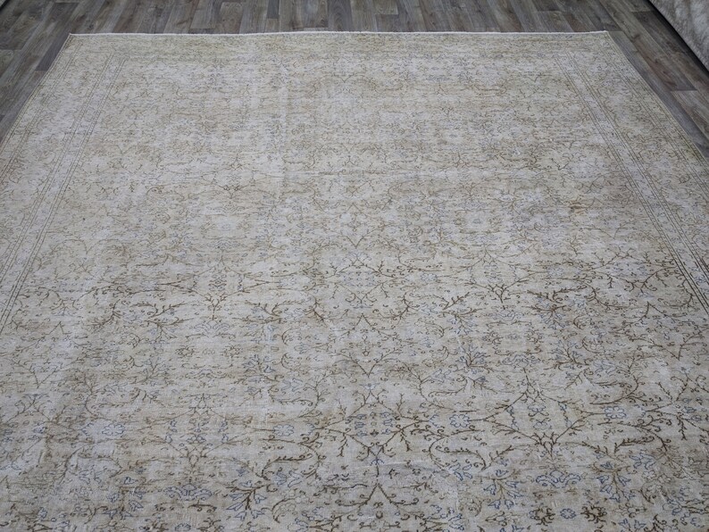 May include: A beige area rug with a light brown and gray floral pattern. The rug has a distressed look and is made of a soft, woven material.