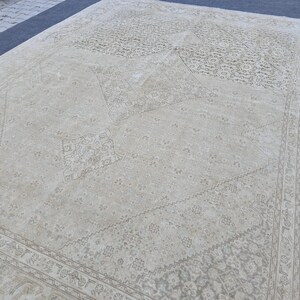 May include: A vintage cream-colored rug with a faded floral pattern. The rug has a diamond-shaped design in the center and a border around the edges.