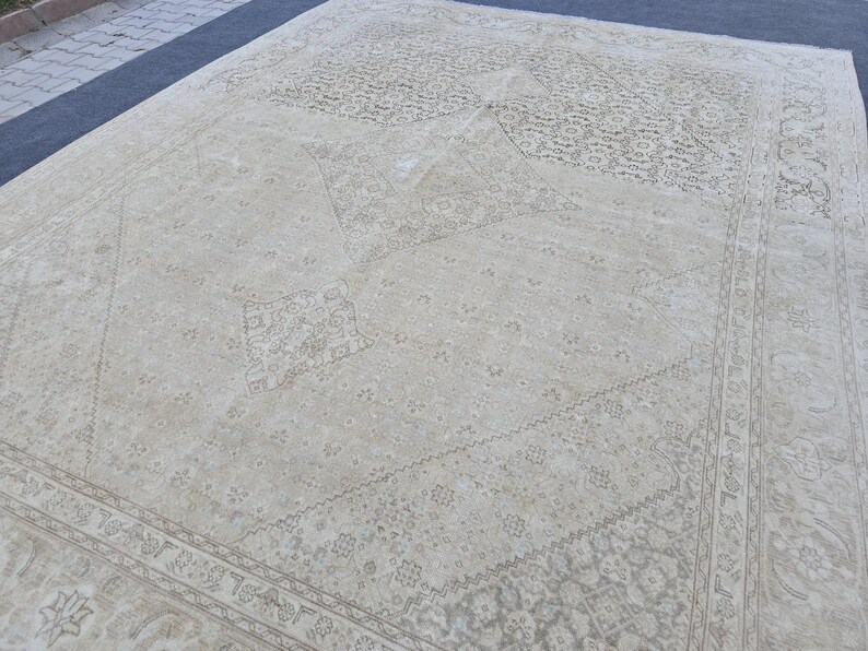 May include: A vintage cream-colored rug with a faded floral pattern. The rug has a diamond-shaped design in the center and a border around the edges.