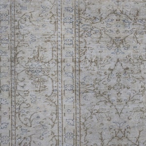 May include: A close-up of a beige rug with a light brown and blue floral pattern. The rug has a distressed look and is made of a soft, woven material.
