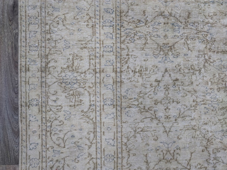 May include: A close-up of a beige rug with a light brown and blue floral pattern. The rug has a distressed look and is made of a soft, woven material.