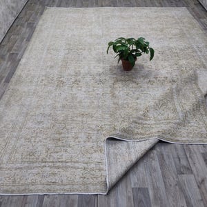 May include: A vintage-style rug with a faded floral pattern in shades of beige and green. The rug is folded in half and laid out on a wooden floor.